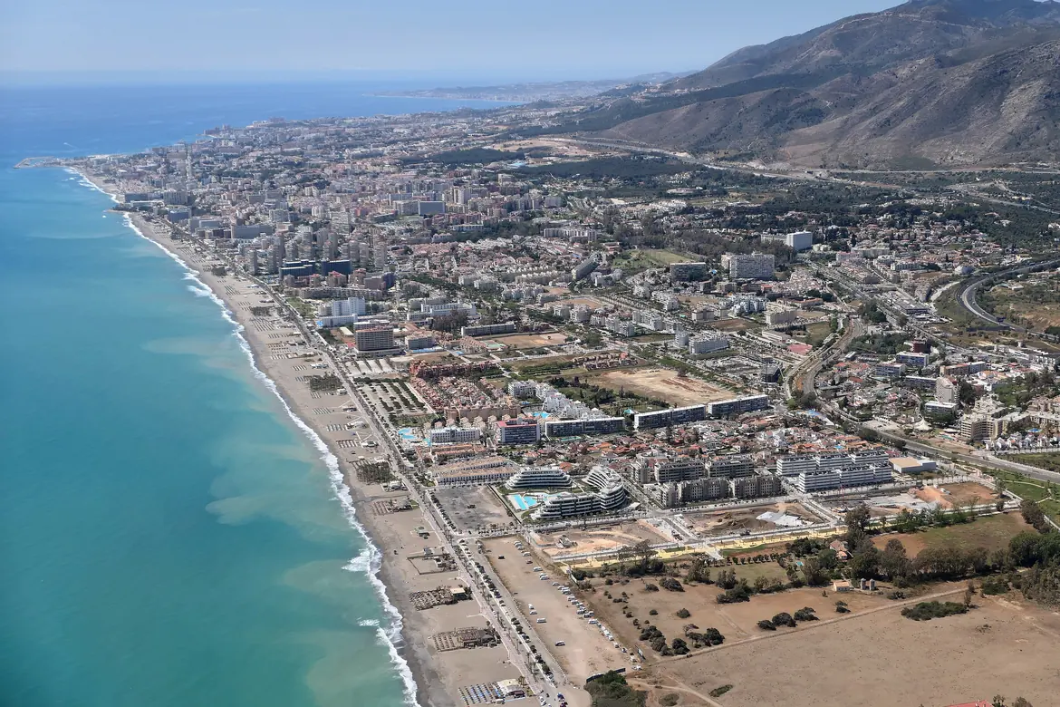 An aerial view of the Torremolinos shoreline, a long beach with the town behind it and a mountain ridge rising in the distance